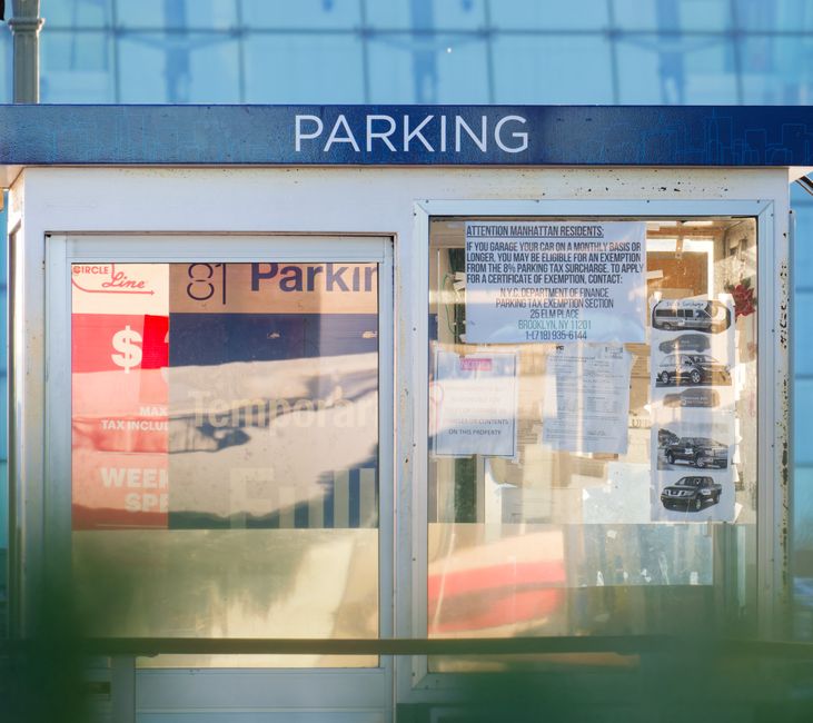 Close-up view of a black wooden wall with vertical planks, featuring a white and red 'No Parking Any Time' sign attached to the surface. The sign has red text and borders, with two red arrows pointing